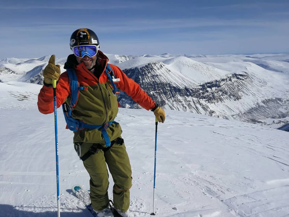 A skier in orange and olive on a ridge in northern Sweden