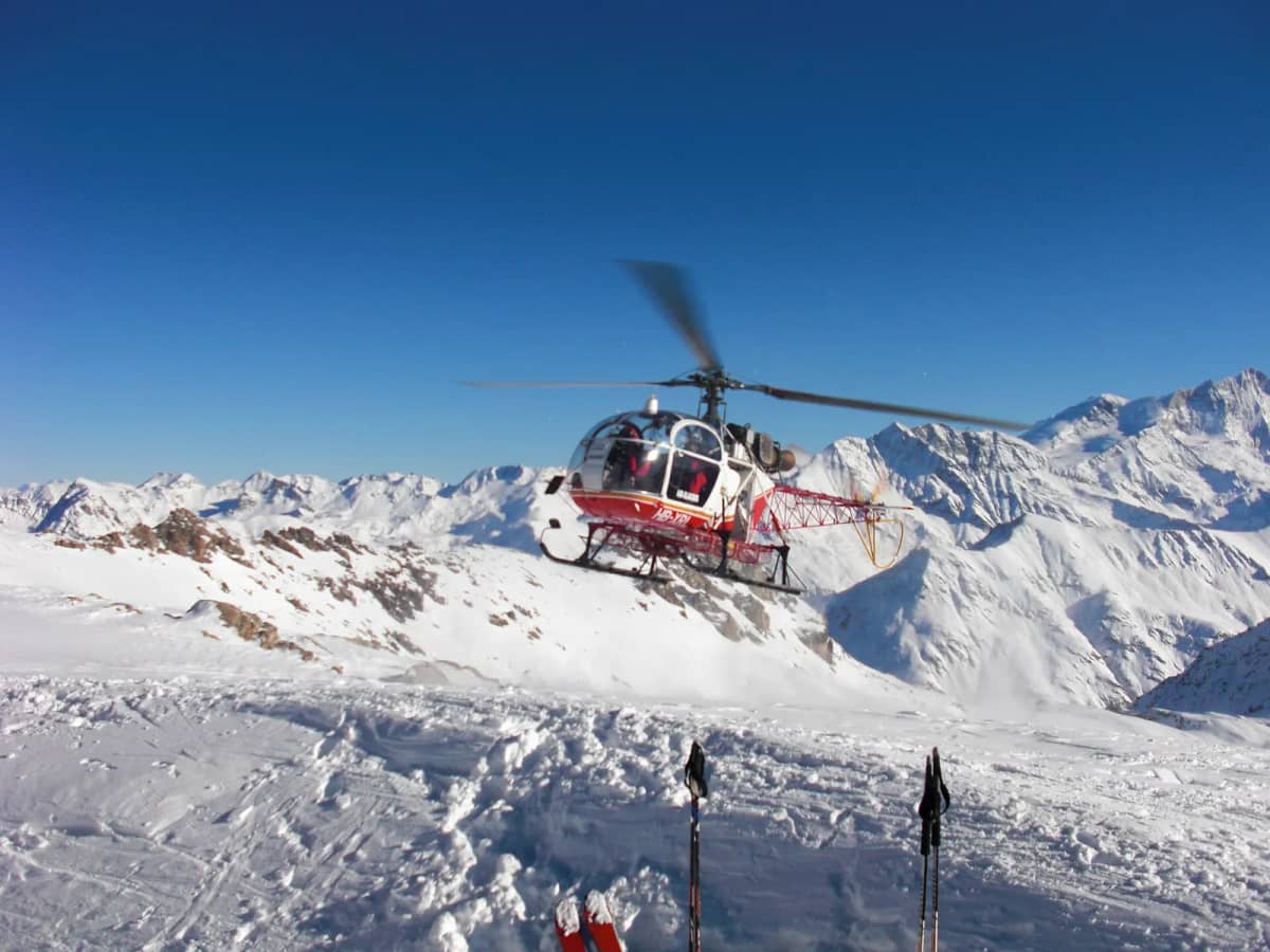 An Air Glaciers helicopter landing on a snowy Swiss ridge, ski poles in the foreground