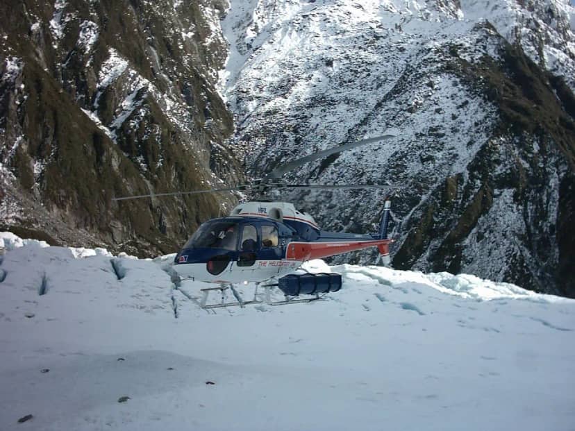 A helicopter landed on snow beside a glacier