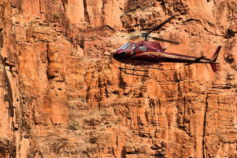 A helicopter flying along a red canyon wall