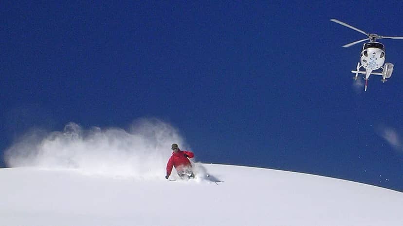 A skier on a powder slope with a helicopter above