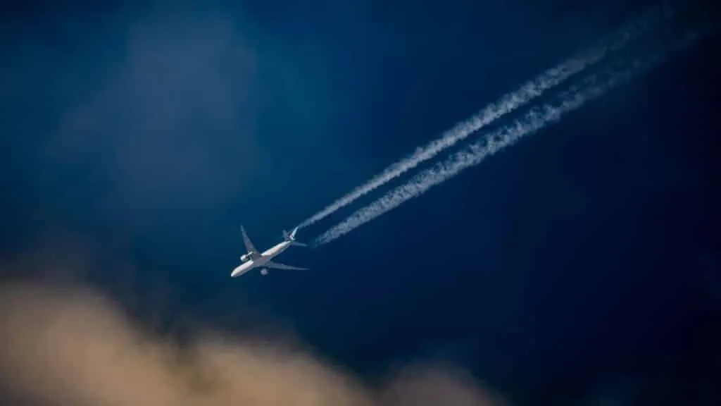 A commercial passenger aircraft flying over a blue sky, leaving a trail of contrails